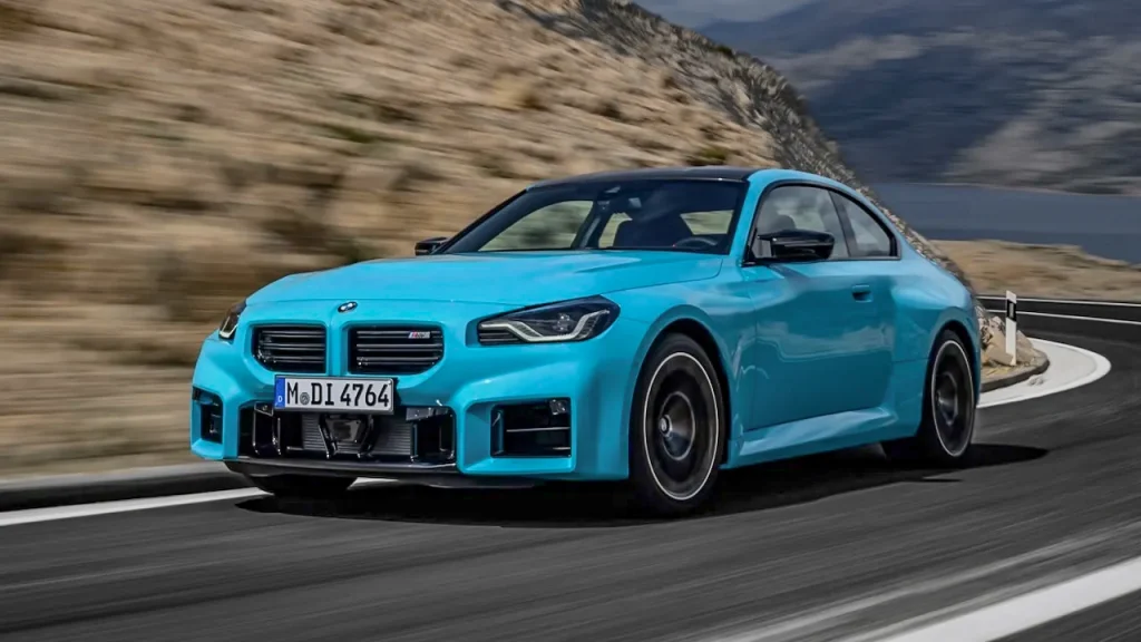 Vista lateral y frontal en movimiento del nuevo BMW M2 xDrive azul en carretera, un coche deportivo de tracción total para importación en Andorra.